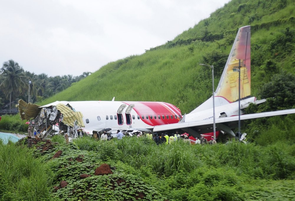 Officials stand on the debris of the Air India Express flight that skidded off a runway while landing in Kozhikode, Kerala state, India, Saturday, Aug. 8, 2020. The special evacuation flight bringing people home to India who had been trapped abroad because of the coronavirus skidded off the runway and split in two while landing in heavy rain killing more than a dozen people and injuring dozens more. (AP Photo/C.K.Thanseer)